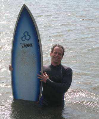 Dr. Guerry Grune, founder of 3rd Rock Sunblock, holding a surfboard on the beach